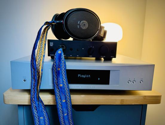 A photo of a network streamer, headphone amplifier and headphones on a bedside table, with a small IKEA lamp in the background.
