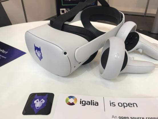 White VR glasses and a couple of controllers laying on a table. The glasses have a Wolvic browser logo sticker in the front.