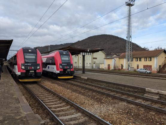Two class 530 South Moravian trains in red-black-white colors at Tišnov station. Květnice hill in the background