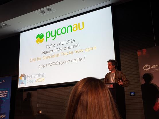 Clinton Roy speaking in front of a slide including "PyConAU, 2025, Naarm Melbourne, Call for Specialist Tracks now open"