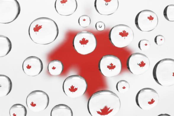 Somewhat abstract composition of water droplets on glass surface, with a printed red maple leaf on white paper several inches underneath the glass. The printed leaf is out of focus, rendering a tiny in-focus maple leaf inside each drop.