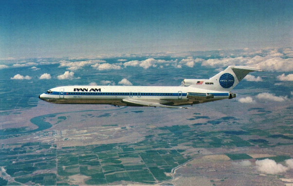 The airplane is flying above fields and clouds from right to left