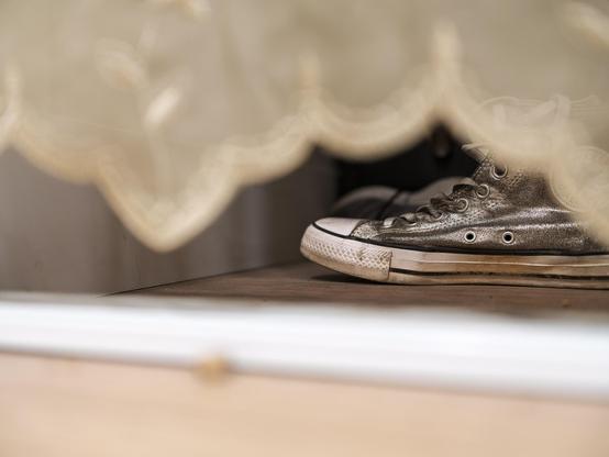 Silver Converse All-Star shoe peeking out from under gauzy curtain.