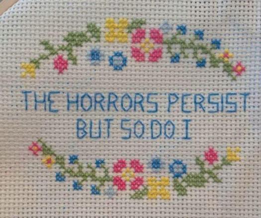A flowery cross stitch that says "the horrors persist, but so do I"