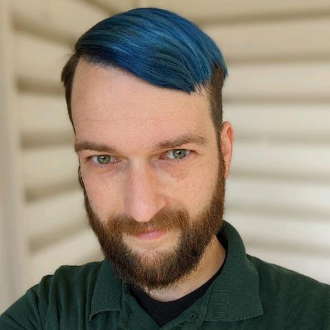 A selfie of a smiling, healthy-looking man with a beard and blue hair