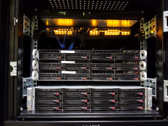A shot of a 1/4 server cabinet with 3 1U compute nodes on top and 4 storage nodes on bottom in a 3U configuration. A network switch is shelved on top with yellow lights.