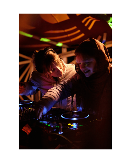 two young people joyfully djing in low key club situation with wooden structures in background