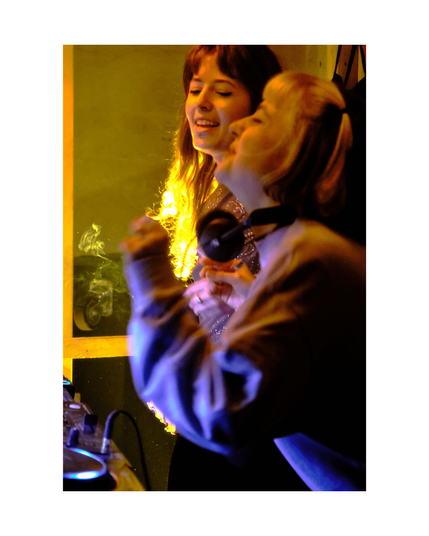 two young people joyfully djing in low key club situation with yellow lighting