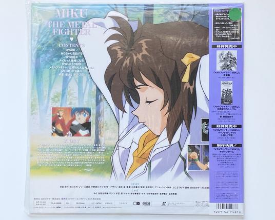 A photo of the back of the laserdisc jacket.  It shows episode details overlaid on top of a big side profile image of Miku with brown hair now.  She's resting against a tree in a forest.