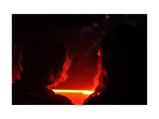 view of silhouettes of back of heads of two young people djing, low key red lighted club situation