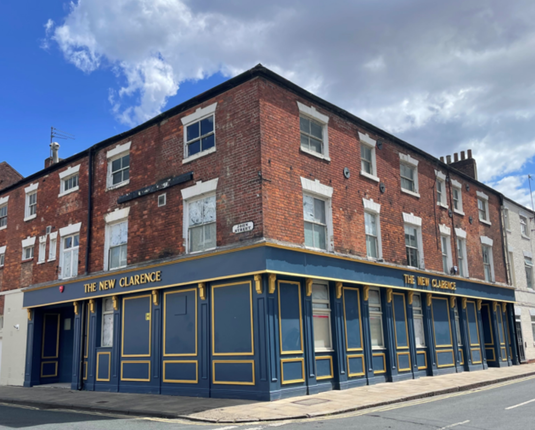 A Georgian brick building with a blue and gold frontage on the corner of a street with a blue sky and a couple of clouds