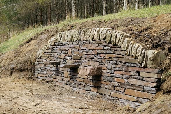 A close, angled view of the wall from the right-hand side. The depth of the wall and the precise fit of the stones are visible. The three bench supports jut out confidently, and the coping stones curve cleanly along the top edge.