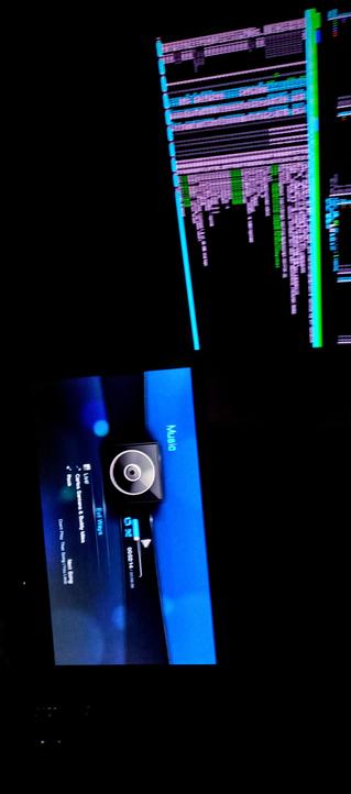 The photograph composed in total darkness shows IPS LED panels side by side. The top screen displays a complex interface with numerous lines of text in various colors, predominantly purple and green, against a black background, the htop program running in bash. The text appears to be a log or data stream, with some horizontal bars in blue and green, possibly indicating different data channels or levels.

The bottom screen shows a music player interface with a blue background. The interface includes a circular control element in the center, with a camera icon to the right. The screen displays the title "Evil Ways" by "Carlos Santana & Buddy Miles," with the genre labeled as "Rock." The time is shown as "09:26:14," and the song is at "1:06:18" in length. The word "Music" is visible at the top of the screen, indicating the current mode of the device.

 Ovis2-8B

🌱 Energy used: 0.219 Wh