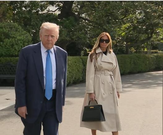 Melania in trench coat next to Trump