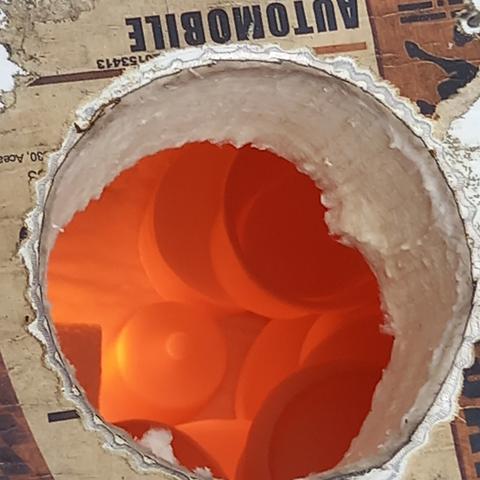 gros plan depuis le trou qui fait office de cheminée du four à raku. On aperçoit des pots rouge vif, témoignage de la chaleur qui règne à l'intérieur du four.