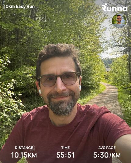 A person wearing a red shirt and glasses is taking a selfie on a wooded path, with details of a running activity overlayed on the image.