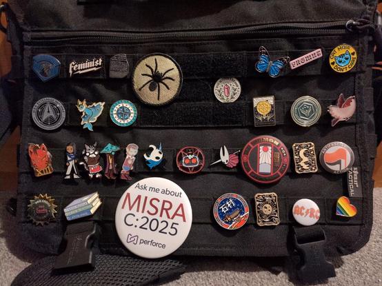 new bag, showing the overflow collection:

timber wolves
Feminist!
rosetta stone
big spider
big witch energy
blue butterfly 
FRGMNT
cat hair don't care
uss enterprise logo
vaporeon
MN north shore
wheel of fortune tarot card
ATREIDES!
a bird (?)
red thirteen
sigmar, dabs, grinderbin, mortimer
ghost of hallownest
cult of the lamb
hornet of hallownest
demon slayer corps
moon tarot card
antifa classic (red+black)
pro books, pro choice, pro feminism
book stack
Ask Me About MISRA C:2025!
usg ishimura
the magician tarot card
AC/RC
rainbow heart