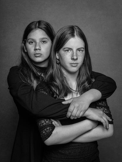 Studioportrait zweier Mädchen, eins umarmt das andere Mädchen von hinten.