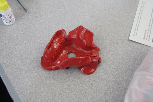 A deep red ceramic poppy on a grey table. One of the petals has signs of cracks in it where it has been glued back together.
