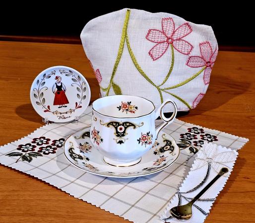 Tea tableau in the style of folk art, with traditional Northern European patterns on china, embroidered linens, and a decorative miniature plate of a Finnish woman in the costume of Hame, Finland. The tea selection is missing because I forgot to include it.