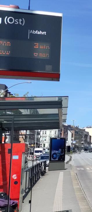 Bushaltestelle Eppendorfer Weg (Ost). Blick in Richtung der ankommenden Busse. Man sieht das FIMS (Fahrtenanzeige), das Dach, den Automaten  ... und eine potthässliche Werbeanlage von JCDecaux, die mitten auf dem Gehweg der Haltestelle prangt.