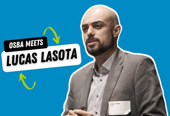 A promotional graphic on a bright blue background showing a man with a shaved head and trimmed beard, wearing a light dress shirt and gray blazer, speaking and holding a presentation clicker. His cut-out figure is outlined in white, and over to the left are two stacked white panels with bold black text reading “OSBA MEETS” and “LUCAS LASOTA,” connected by two green curved arrows.