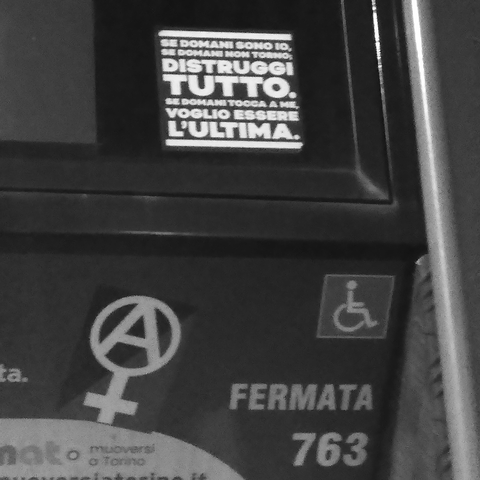 Two stickers on a bus stop time board in Turin. One is a female symbol with the A as Anarchy inscribed in it. The other is a short political message in Italian: 'Se domani sono io, se domani non torno, distruggi tutto. Se domani tocca a me, voglio essere l'ultima.