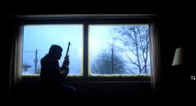 Screenshot aus der Netflix Serie Eternaut. Der Schatten eines Mannes mit Gewehr vor einem hell erleuchteten Fenster mit Schneelandschaft.