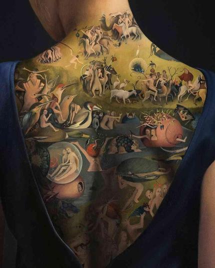 close up of a woman's back with a detailed, intricate artwork tattoo depicting The Garden of Earthly Delights.