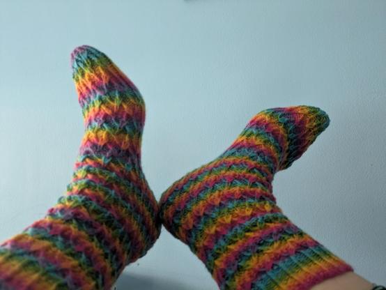 Two feet wearing rainbow striped socks with a rippled texture