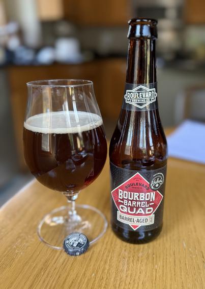 A snifter glass of ruby red ale next to a brown bottle with a red diamond shaped label