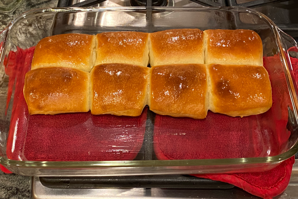 eight buttered rounded rectangular rolls still in their glass baking pan, nice golden brown tops, shiny from freshly applied butter.