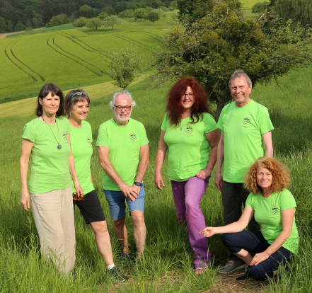 Sechs lächelnde Menschen zwischen 50 und 75 in giftgrünen Geopark-T-Shirts vor grüner Landschaft