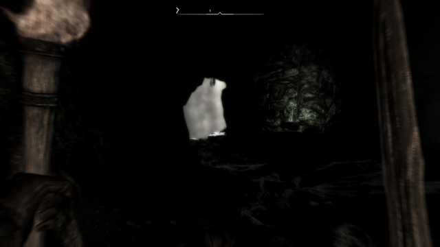Screenshot in Skyrim, inside a cave, holding a torch and a sword. It's really dark. There's an entrance to another room that looks like is blocked by a fog wall ( it's not ).