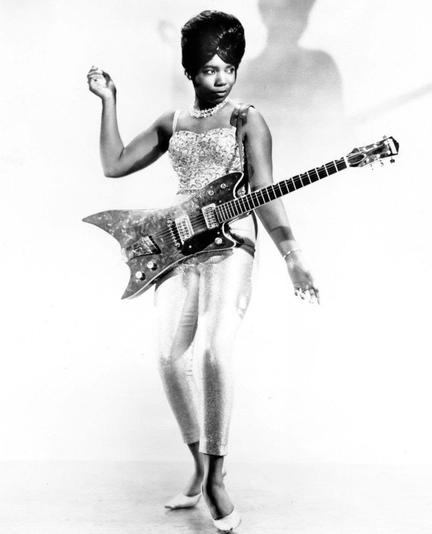 Photo noir et blanc de Norma-Jean Wofford, sur fond blanc, sa guitare électrique en bandoulière.