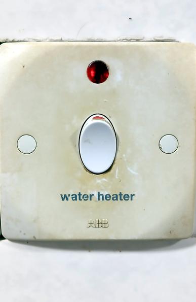 A white plastic switch, soiled from use, with a red light above it, and the words 'water heater' below.