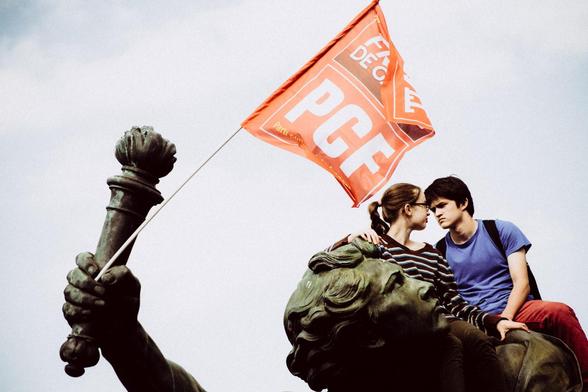 Deux jeunes lycéens se regardent, juchés sur une statue de la place de la Nation. La statue tient un drapeau rouge du PCF qui flotte au dessus d'eux.