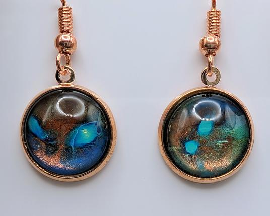A pair of paint dip earrings: the settings are rose gold, and the dipped cabochons are blue, copper, turquoise, and yellow with circular-esque shapes.