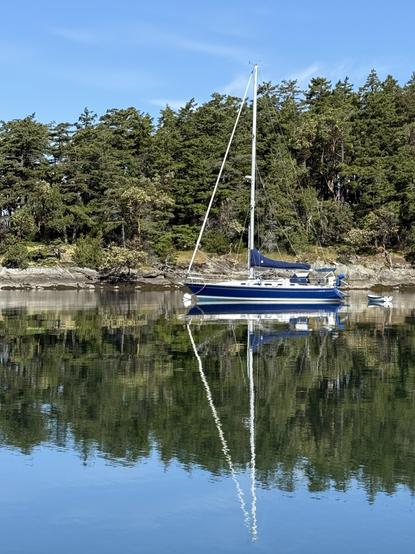 Photograph of a blue and white sailboat on calm water. The entire boat, including its mast and rigging, and the forested shoreline behind him, reflect perfectly in the still water. The sky is blue with just a few wispy clouds.

This photo copyright 2025 by Maria Langer. All rights reserved. Neither this image nor the accompanying alt text may be used to train AI systems.