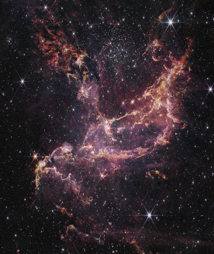 Picture of a nebula, almost an X in shape, shown in pinks and oranges against a backdrop of deep space.