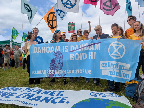 Aktivistengruppe mit bunten XR-Fahnen und hellblauem XR-Banner
"DAHOAM IS BOID HI
KLIMAKRISE MITEINAND STOPPEN"