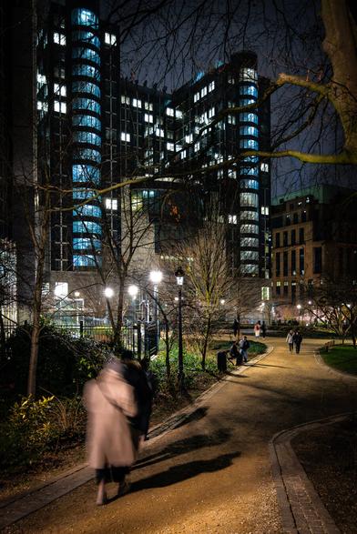Silhouettes of people going down walking in the Leopold Park in Brussels at night with the illuminated building of the European Parliament in the background.