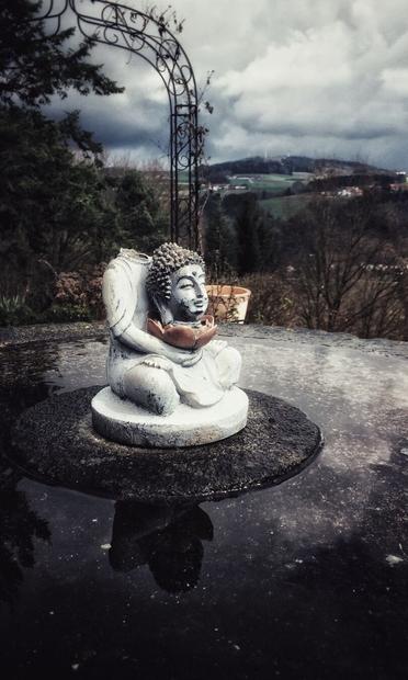 A small Buddha statue sitting on an old mill stone with the head separated from the Buddhas body and placed on the lotus flower the statue is holding in their hands