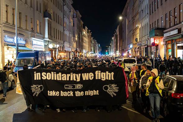 Das Foto von © Björn Obmann zeigt die Demo mit dem Fronttranspi "In Solidarity we fight - take back the Night" und den dahinter laufenden schwarzen Block, gefolgt von vielen anderen Menschen.