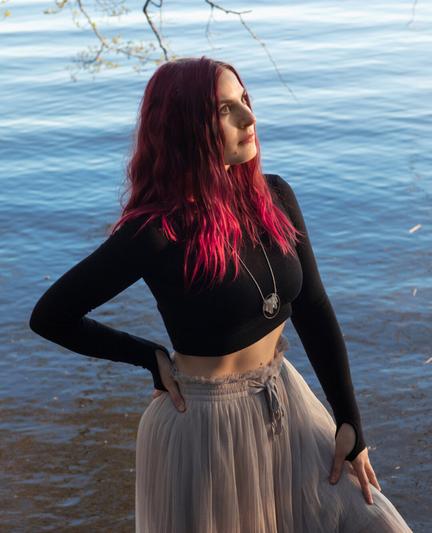A finnish woman wearing a croptop and a tulle skirt posing in front of a lake