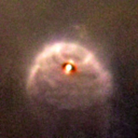 What looks to be a bright star is surrounded by a flattened circle of gas and dust, rippling outward.