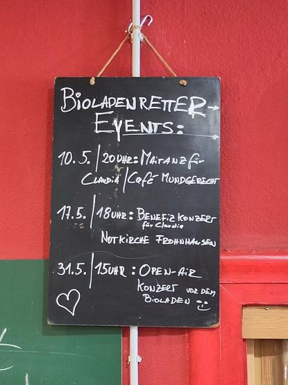 Schwarze Tafel an einer roten Wand. Darauf stehen in weißer Kreideschrift Termine:
Bioladenretter-Events:
10.05. / 20 Uhr: Maitanz für Claudia / Café Mundgerecht
17.05. / 18 Uhr: Benefizkonzert für Claudia / Notkirche Frohnhausen
31.05. / 15 Uhr: Open-Air-Konzert vor dem Bioladen