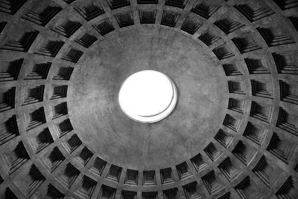 A low-angle, black and white shot of the interior dome of the Pantheon in Rome, Italy, featuring a central circular opening to the bright sky, surrounded by a grid of recessed square panels.