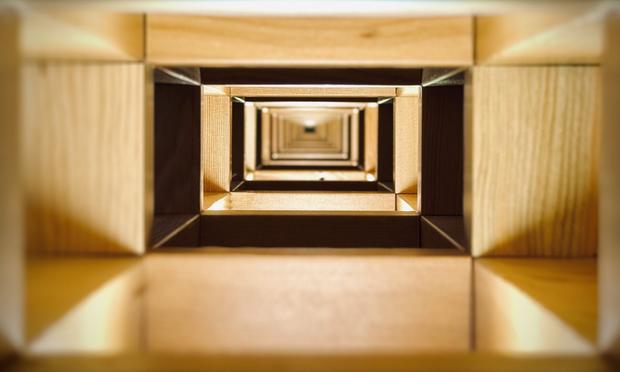 A perspective view through wall framework reveals a seemingly endless tunnel of two-by-four and four-by-four rectangular wooden supports, each unique section lit from underneath by individual incandescent bulbs.