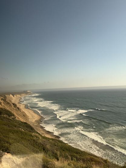 looking down from the top of a cliff (on the train) at low waves breaking along a beach.